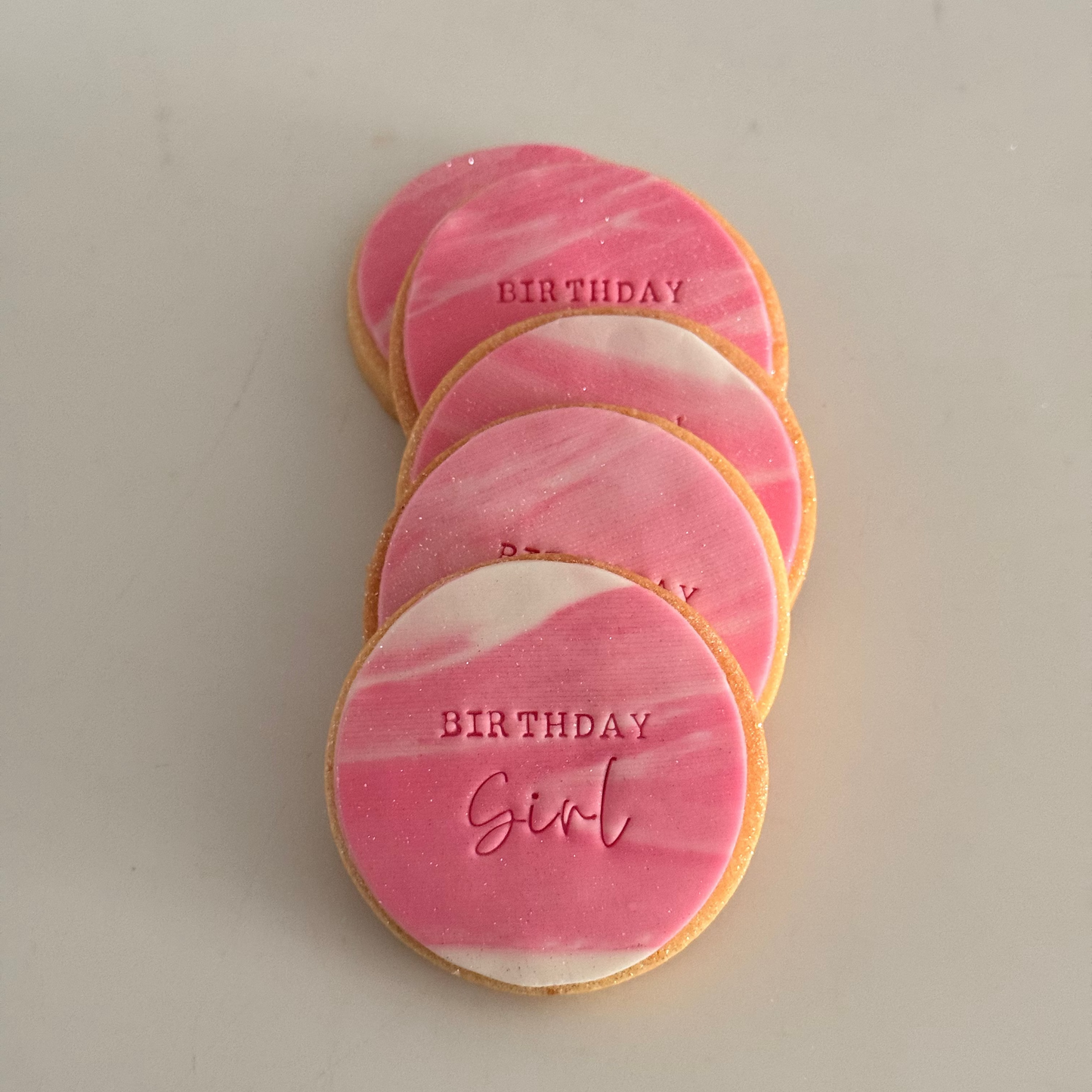 birthday cookies with pink and white marbled icing stamped with the text 'BIRTHDAY Girl'