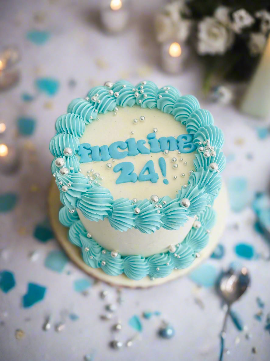 mini cake with fucking 24 words on top in baby blue, finished with shiny silver sprinkles