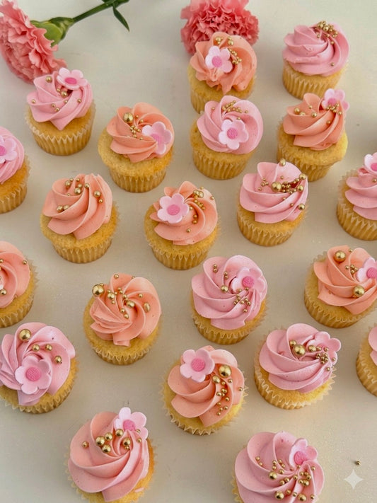 mini vanilla cupcakes with pink & peach frosting and decorative elements on a light background