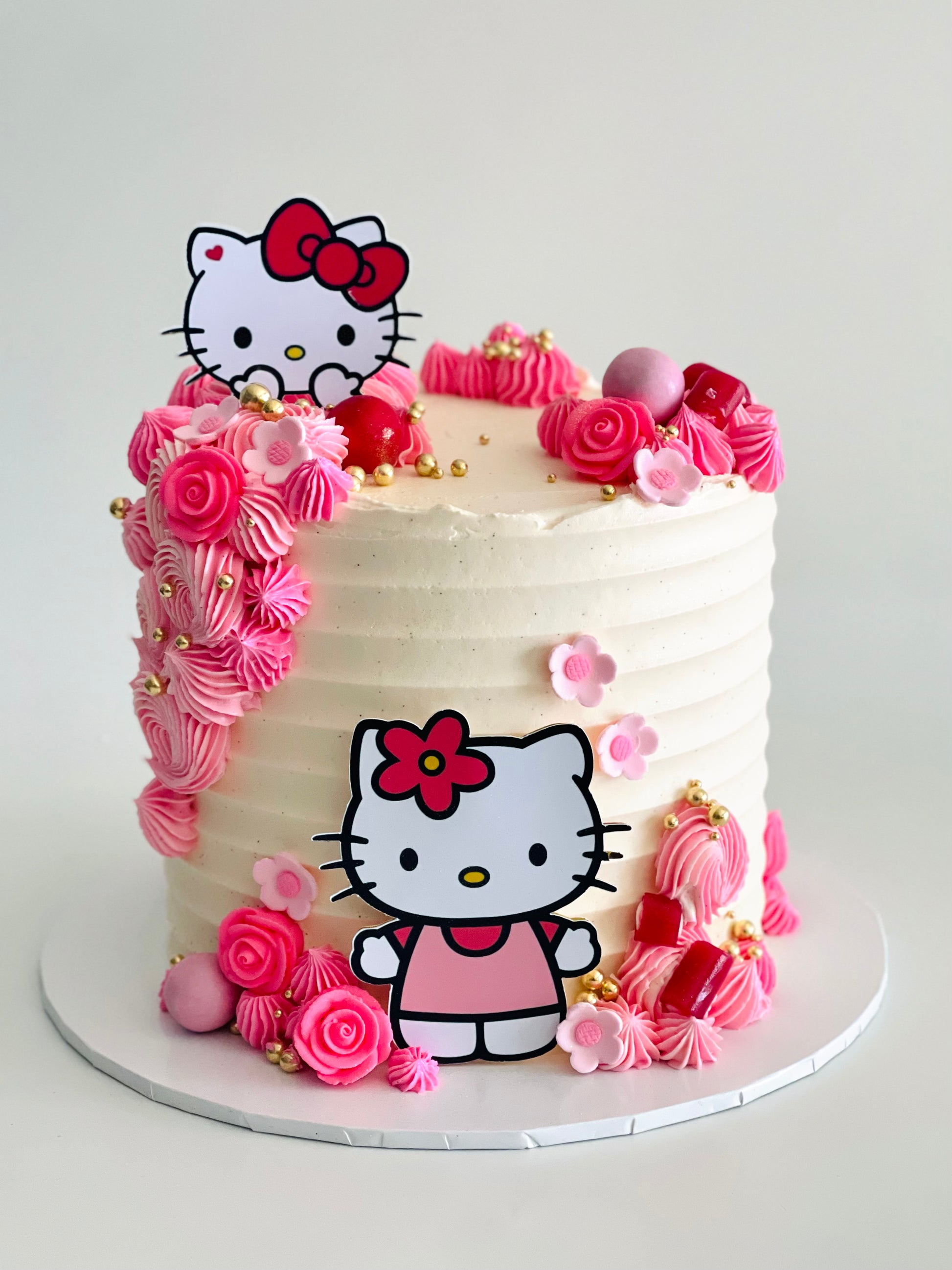 A Hello Kitty themed cake decorated with white and pink icing, and Hello Kitty character figurines on top.
