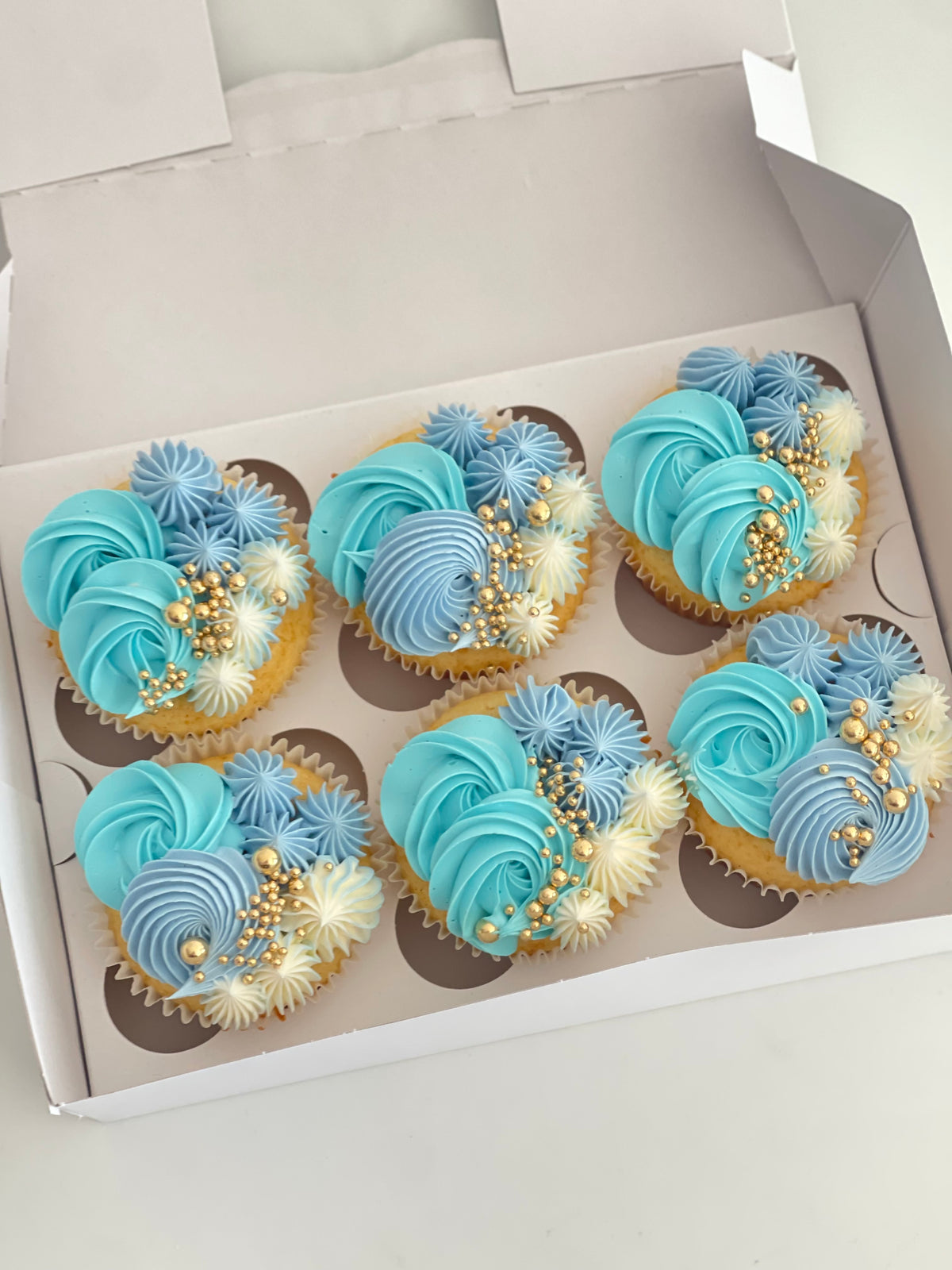 Box of cupcakes with blue and white frosting in a decorative pattern