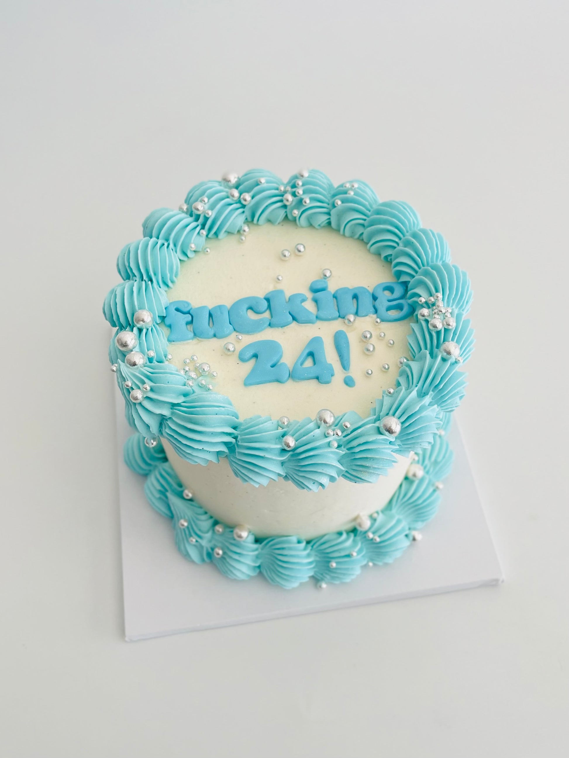 mini cake with fucking 24 words on top in baby blue, finished with shiny silver sprinkles